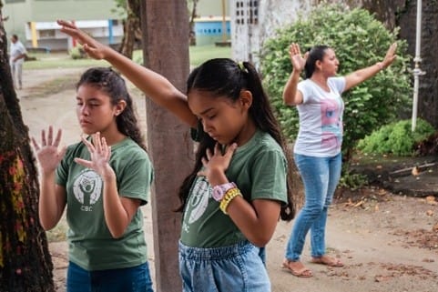 Teacher and two students praying in school grounds.